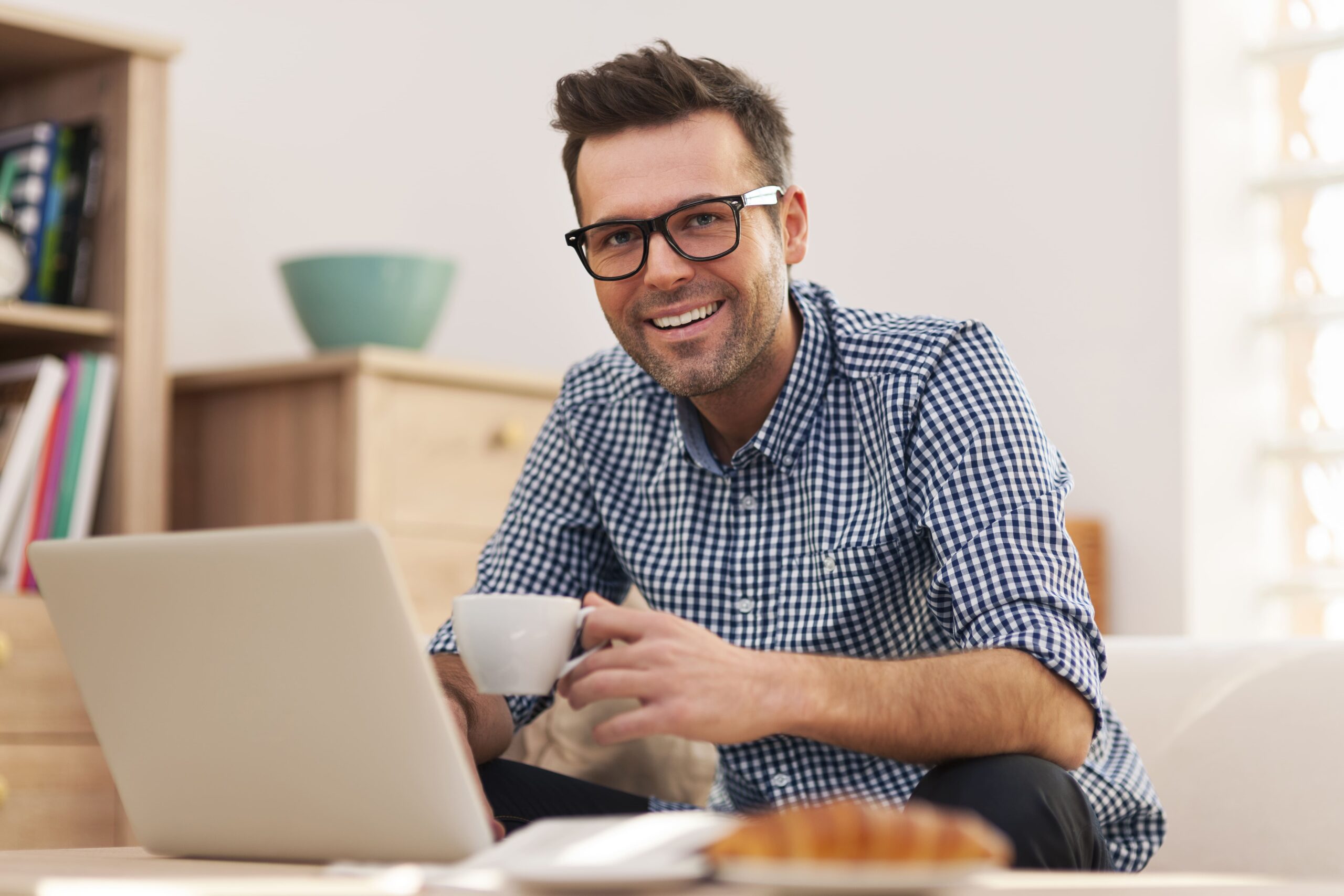 Profissional sorrindo com uma xícara de café diante do notebook